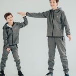 Two brothers sharing a high-five in matching gray outfits on a white background. Studio captured.