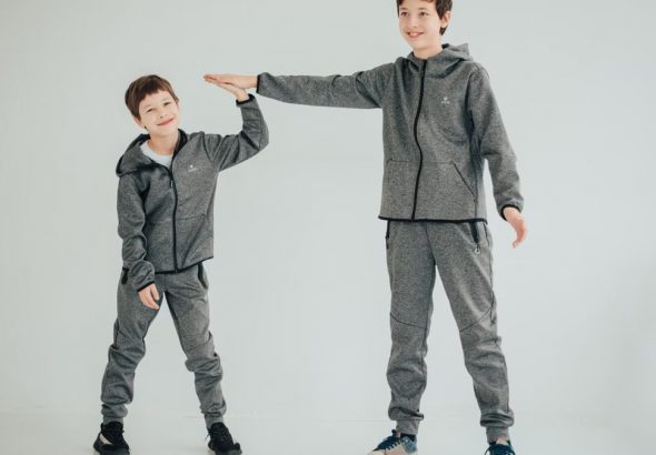 Two brothers sharing a high-five in matching gray outfits on a white background. Studio captured.