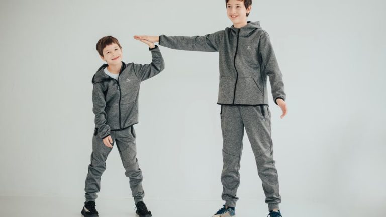 Two brothers sharing a high-five in matching gray outfits on a white background. Studio captured.