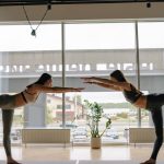 Two women performing yoga poses in a contemporary indoor studio.